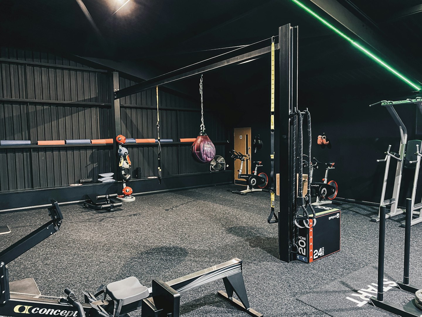 Moderner Fitnessraum mit Rudergerät, Boxsack und Fahrrädern.